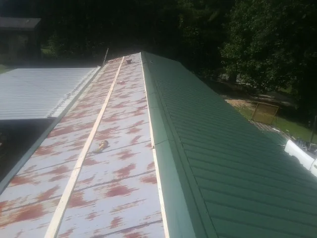 Old rusted panels beside newly installed green metal roofing — Wind Damage Roof Repair by Roofing Brothers in Capitol Heights