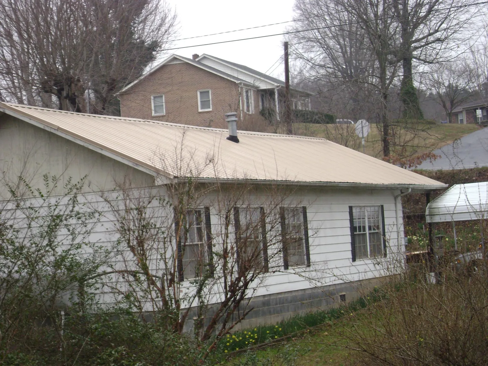 Tan metal roof on a white sided house set into a hillside — Commercial Roofing by Roofing Brothers in Capitol Heights